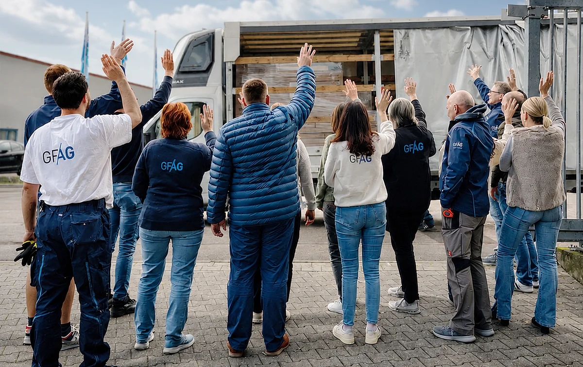 Gelebte Unternehmenswerte bei der GFAG: Ein Teil des Teams steht von hinten zu sehen auf dem Werksgelände und winkt geschlossen einem beladenen Lkw hinterher. Das Bild symbolisiert Zusammenhalt, gemeinsame Erfolge und den Stolz auf die erbrachte Leistung.