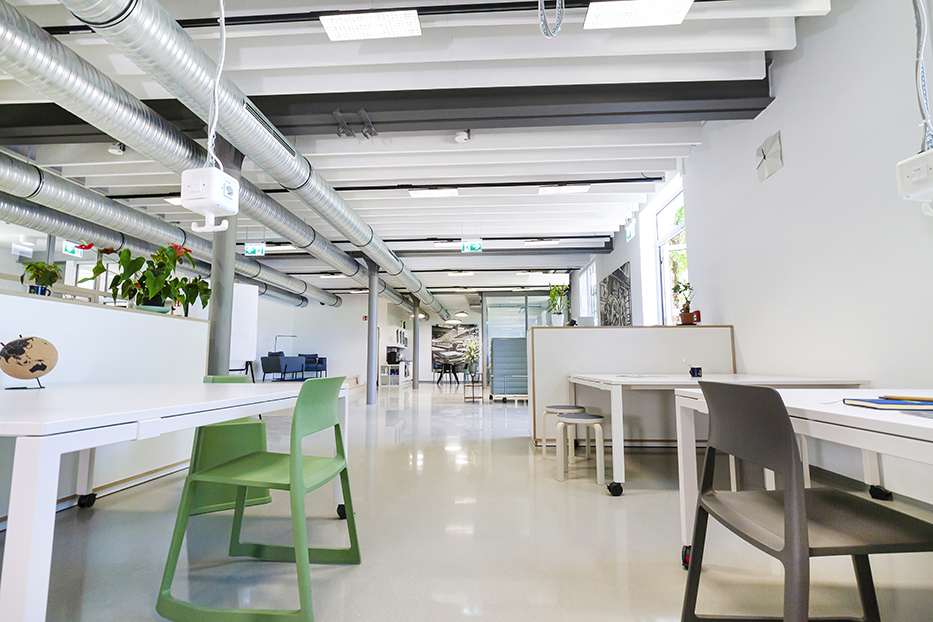GFAG-Projektreferenz im Dock 33: Perspektivischer Blick durch das helle Open-Space-Büro mit Fokus auf moderne Arbeitsplätze im Vordergrund. Die weißen Akustikbaffeln an der Decke ziehen sich elegant durch den gesamten Raum und fügen sich harmonisch zwischen Industrie-Lüftungsrohren und Deckenelementen ein.