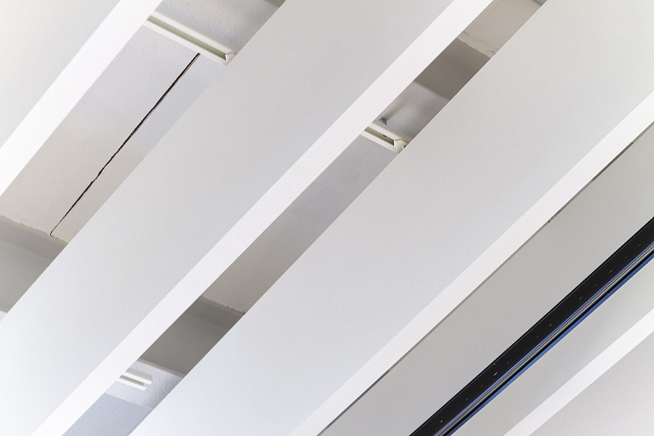 GFAG-Projektreferenz im Dock 33: Detailansicht der deckenabgehängten, weißen Akustikbaffeln. Das Bild zeigt die lineare, parallele Anordnung der schallabsorbierenden Lamellen und verdeutlicht, wie unauffällig moderne Technik und Lichtleisten in das Akustiksystem integriert werden können.